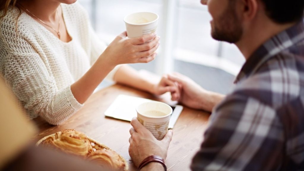 twee mensen die genieten van koffie en elkaars hand vasthouden
