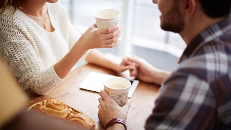 twee mensen die genieten van koffie en elkaars hand vasthouden