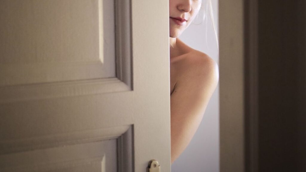 Het naakte lichaam van een vrouw gluurt achter een deur